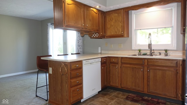 kitchen with brown cabinets, light countertops, a sink, dishwasher, and a peninsula