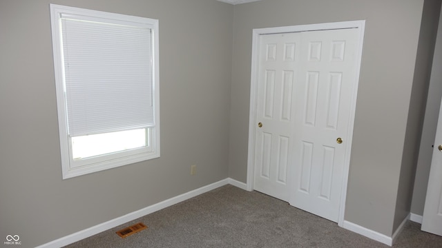 unfurnished bedroom with baseboards, visible vents, dark carpet, and a closet