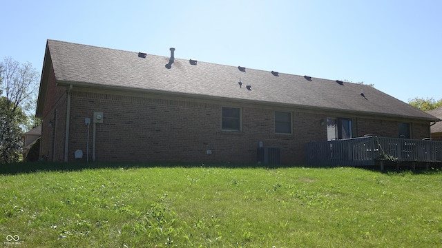 back of house with roof with shingles, brick siding, a lawn, and cooling unit