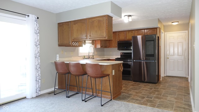 kitchen with brown cabinets, light countertops, appliances with stainless steel finishes, a sink, and a peninsula