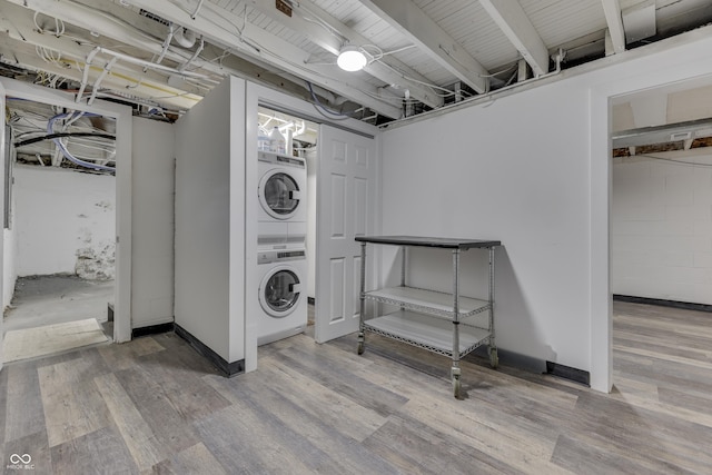 laundry area with stacked washer and dryer, laundry area, baseboards, and wood finished floors