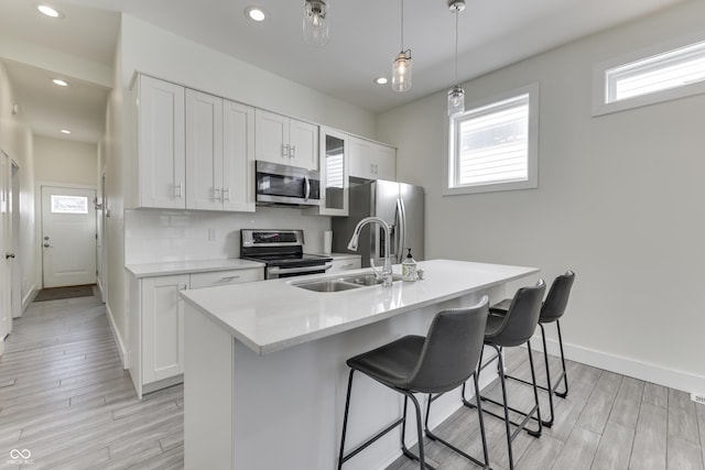 kitchen with a breakfast bar, a sink, light countertops, appliances with stainless steel finishes, and tasteful backsplash