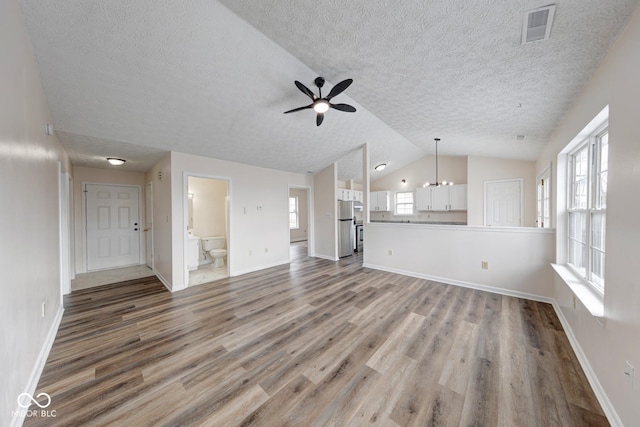 unfurnished living room with lofted ceiling, visible vents, ceiling fan, wood finished floors, and baseboards