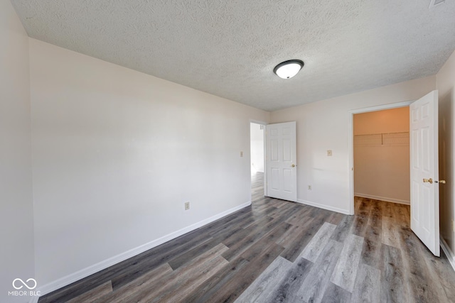 unfurnished bedroom with baseboards, dark wood finished floors, a walk in closet, a textured ceiling, and a closet