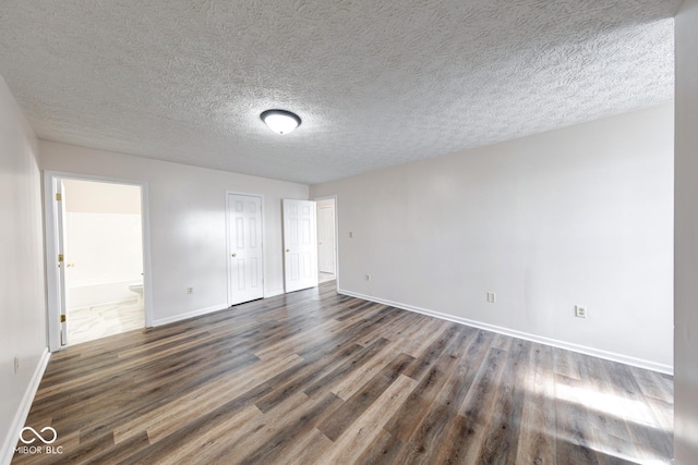 spare room with dark wood-style floors, a textured ceiling, and baseboards