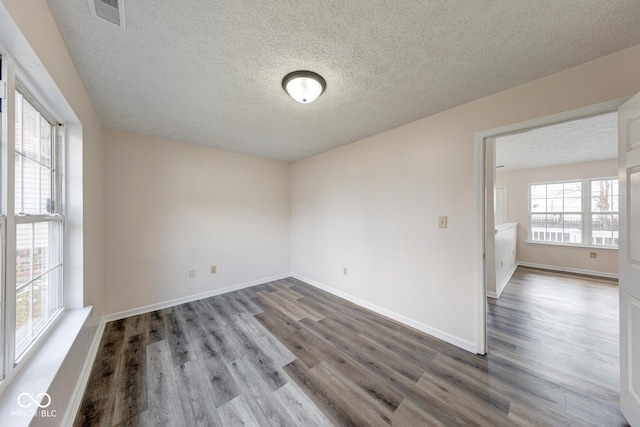 empty room featuring visible vents, a textured ceiling, baseboards, and wood finished floors