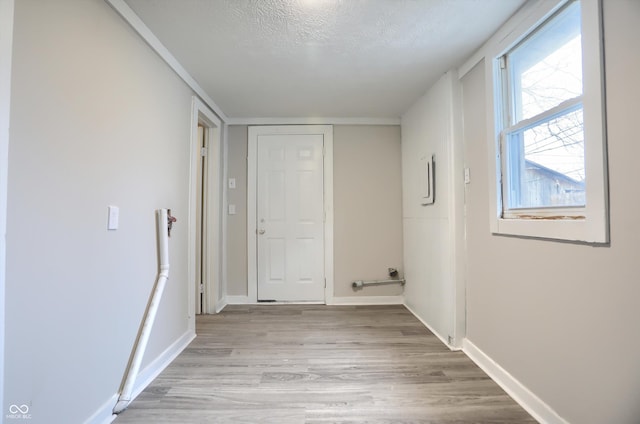 hallway featuring baseboards, a textured ceiling, and light wood finished floors