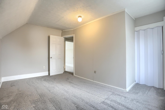 interior space featuring baseboards, a textured ceiling, carpet flooring, and vaulted ceiling