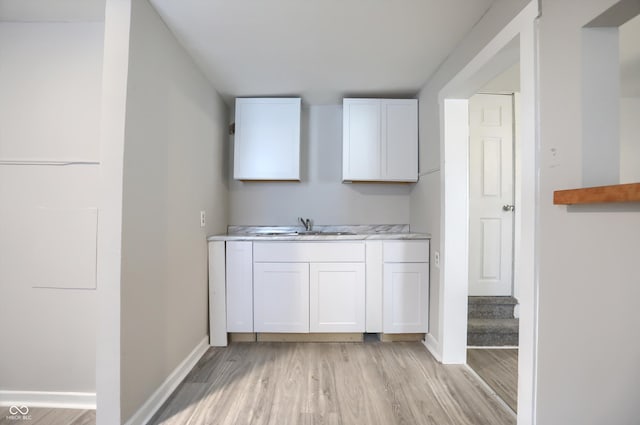 bar featuring a sink, light wood-type flooring, and baseboards