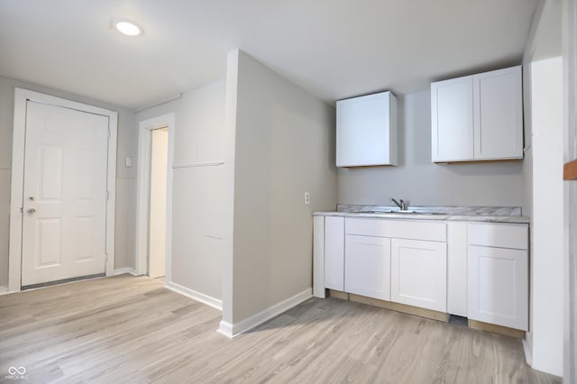 kitchen featuring light wood-style flooring, white cabinets, light countertops, and a sink