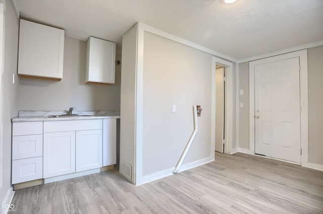 kitchen featuring a sink, baseboards, white cabinets, and light wood finished floors