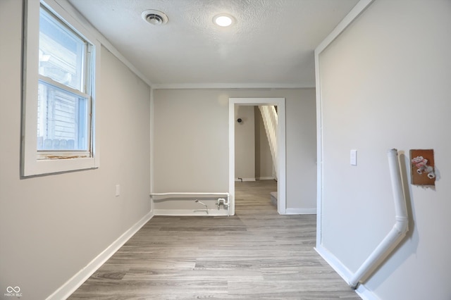 spare room featuring light wood-type flooring, visible vents, baseboards, and a textured ceiling