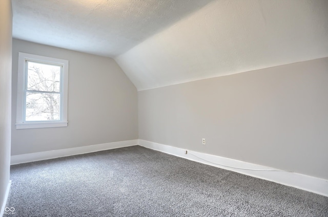 additional living space with baseboards, a textured ceiling, lofted ceiling, and dark colored carpet