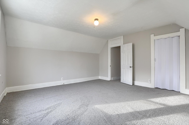 additional living space featuring vaulted ceiling, carpet flooring, baseboards, and a textured ceiling