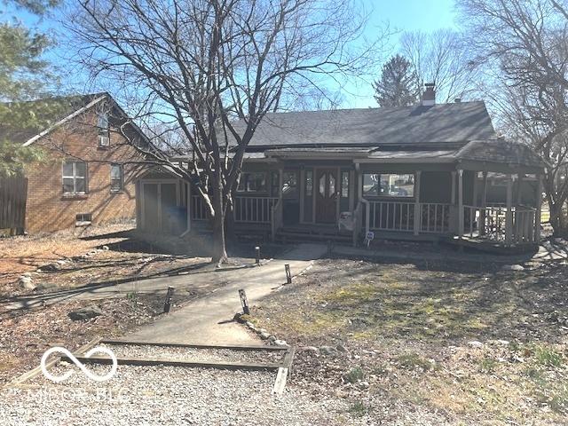 view of front of home with covered porch, a chimney, and brick siding