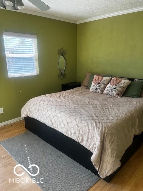 bedroom featuring crown molding, a textured ceiling, baseboards, and wood finished floors