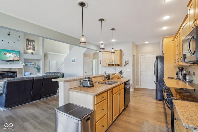 kitchen with black appliances, light wood-style flooring, a tiled fireplace, a sink, and open floor plan