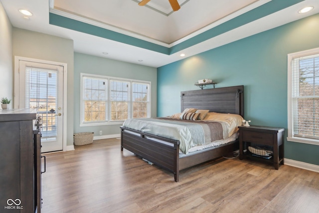 bedroom with a raised ceiling, recessed lighting, wood finished floors, and baseboards