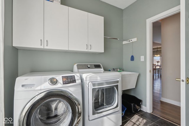 laundry room with dark tile patterned flooring, baseboards, washer and dryer, cabinet space, and a sink