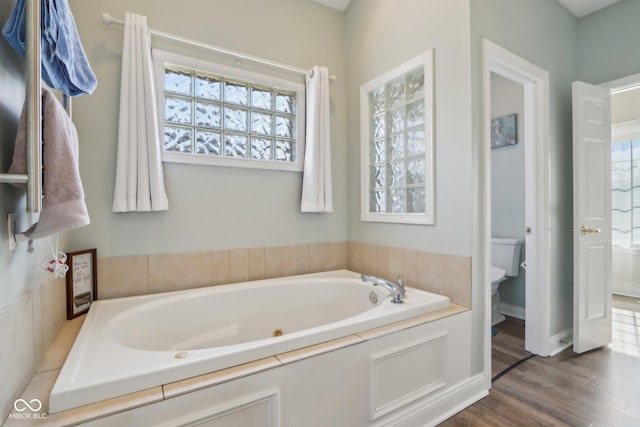 full bathroom with toilet, a tub with jets, and wood finished floors