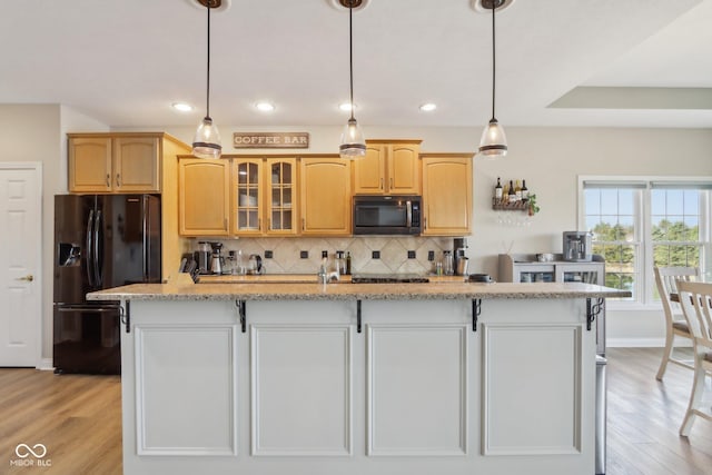 kitchen with decorative backsplash, light wood-style floors, a kitchen island with sink, and black refrigerator with ice dispenser