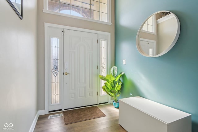 foyer entrance with visible vents, a high ceiling, baseboards, and wood finished floors