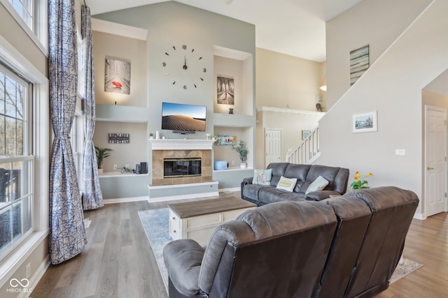 living area with stairway, built in shelves, wood finished floors, a towering ceiling, and a tiled fireplace