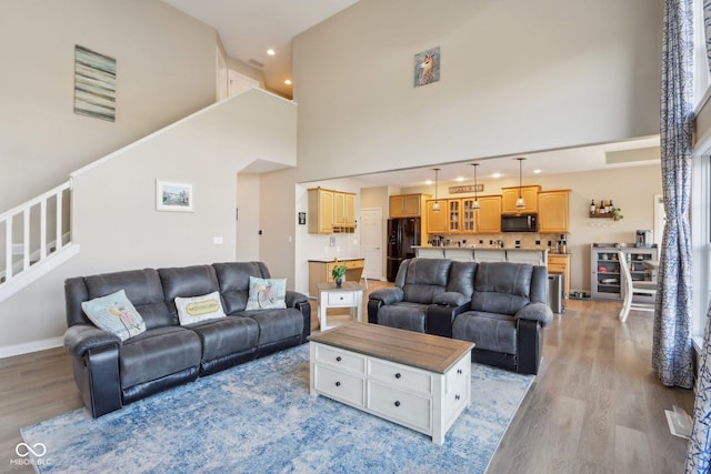 living room with wine cooler, a towering ceiling, stairs, and light wood finished floors