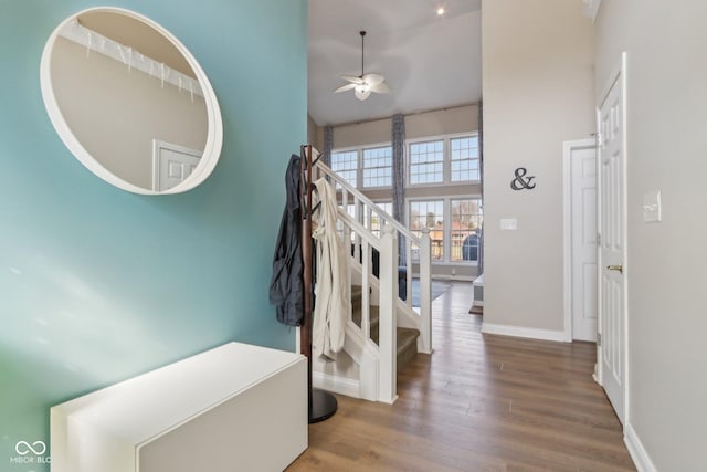 staircase featuring baseboards, a high ceiling, a ceiling fan, and wood finished floors