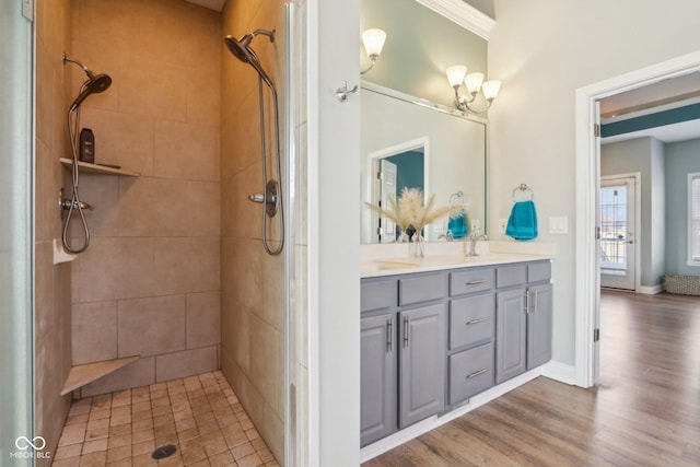 bathroom featuring double vanity, baseboards, tiled shower, and wood finished floors