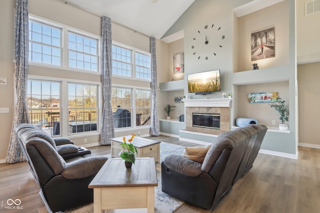 living room featuring wood finished floors, baseboards, visible vents, high vaulted ceiling, and a fireplace