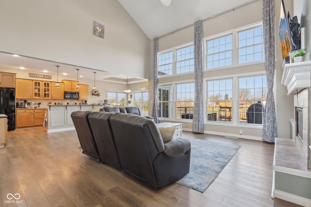 living area with baseboards, high vaulted ceiling, light wood-style flooring, and a fireplace