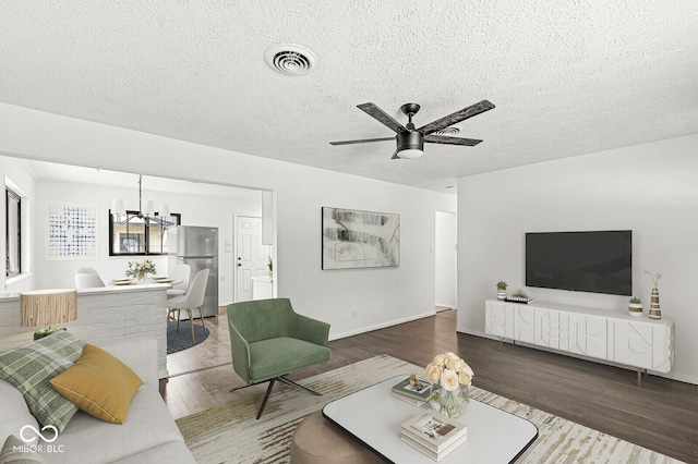 living area with visible vents, baseboards, ceiling fan with notable chandelier, wood finished floors, and a textured ceiling