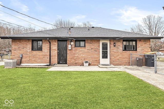 back of house with a lawn, a shingled roof, brick siding, and fence