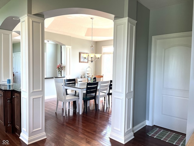 dining space with dark wood-style flooring, a raised ceiling, and ornate columns