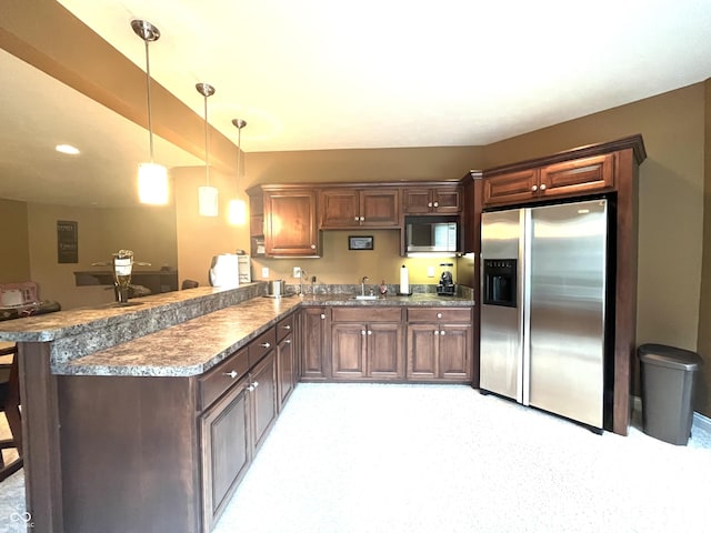 kitchen featuring a peninsula, stainless steel refrigerator with ice dispenser, a sink, and decorative light fixtures