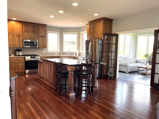 kitchen featuring a breakfast bar, a sink, appliances with stainless steel finishes, a center island, and dark wood-style floors