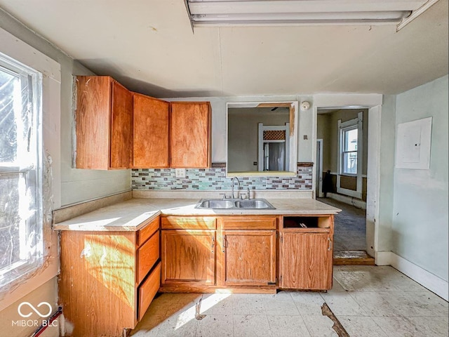 kitchen featuring brown cabinets, a sink, electric panel, tasteful backsplash, and light countertops