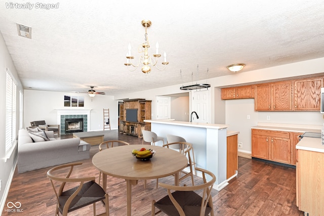 dining room with ceiling fan with notable chandelier, a textured ceiling, dark wood finished floors, a fireplace, and baseboards