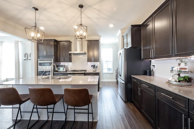 kitchen featuring a breakfast bar, ornamental molding, a sink, appliances with stainless steel finishes, and wall chimney range hood