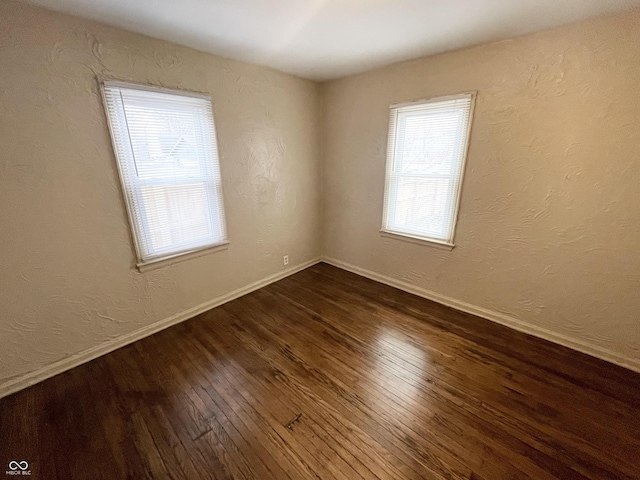 spare room with baseboards, dark wood finished floors, and a textured wall