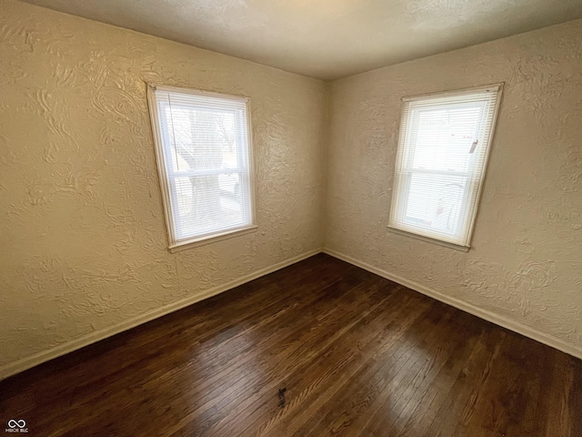 unfurnished room featuring baseboards, dark wood-style floors, and a textured wall