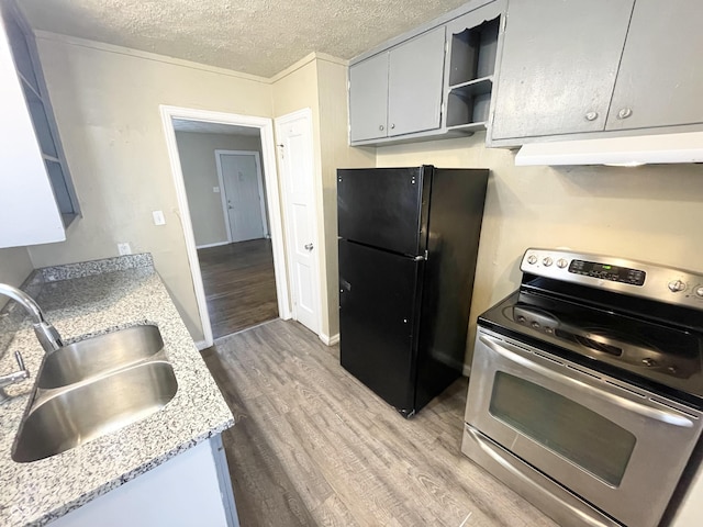 kitchen featuring light wood-type flooring, stainless steel range with electric stovetop, under cabinet range hood, a sink, and freestanding refrigerator