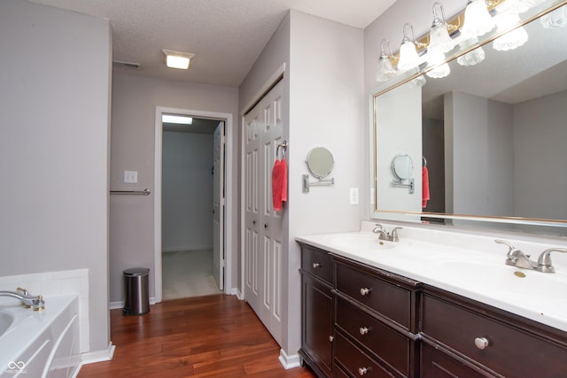 full bath with a bath, a textured ceiling, a sink, and wood finished floors