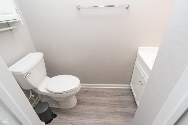 bathroom featuring toilet, baseboards, wood finished floors, and vanity