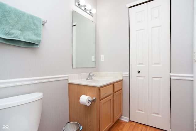 half bath featuring toilet, a wainscoted wall, wood finished floors, vanity, and a closet