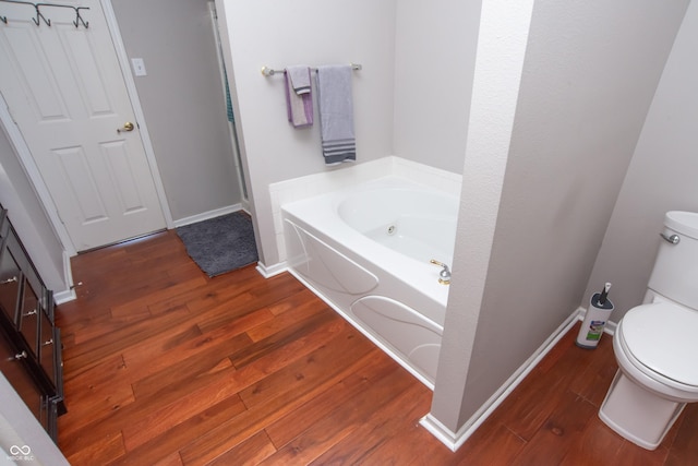 bathroom featuring a tub with jets, wood finished floors, toilet, and baseboards