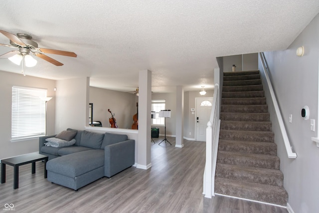 living room featuring a textured ceiling, stairway, light wood-style flooring, and a ceiling fan