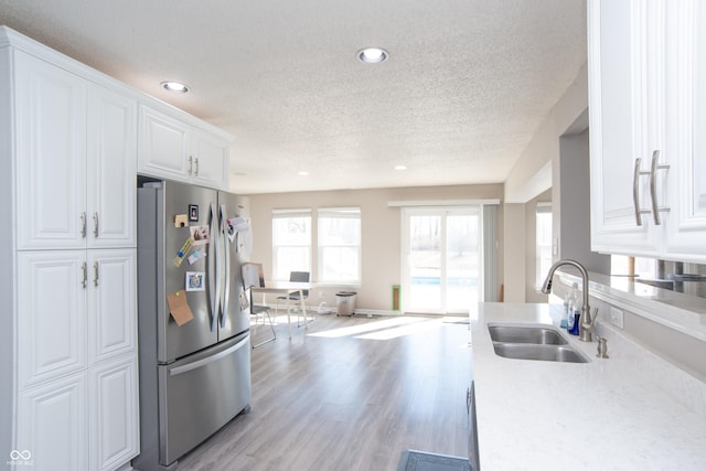 kitchen featuring freestanding refrigerator, light countertops, light wood-style floors, white cabinetry, and a sink