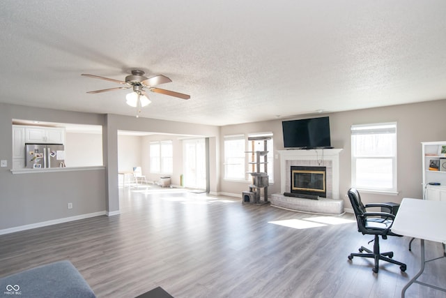 home office with ceiling fan, a textured ceiling, wood finished floors, baseboards, and a glass covered fireplace